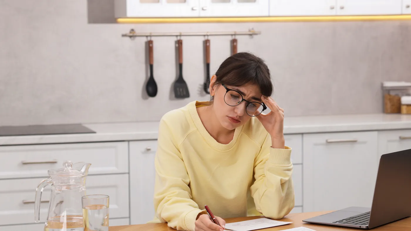 A woman at her kitchen table working through a stack of bills with a calculator